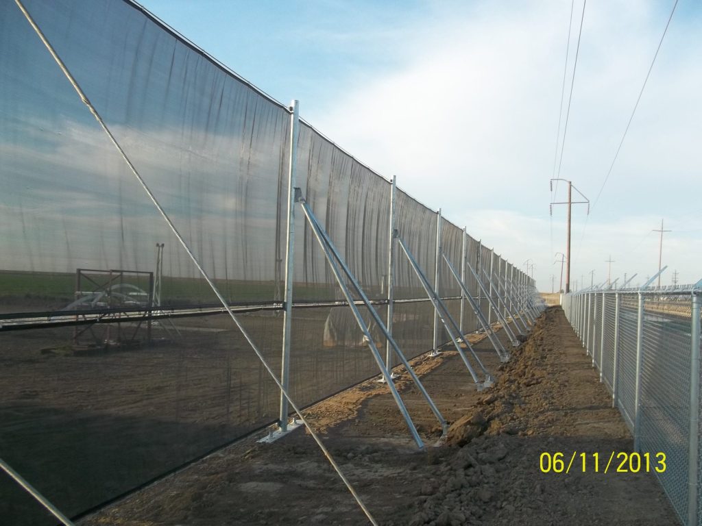 A long line of metal fencing with angled supports and dark mesh screens
