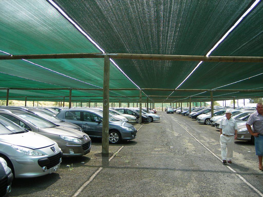 Cars parked under a large green canopy supported by wooden poles
