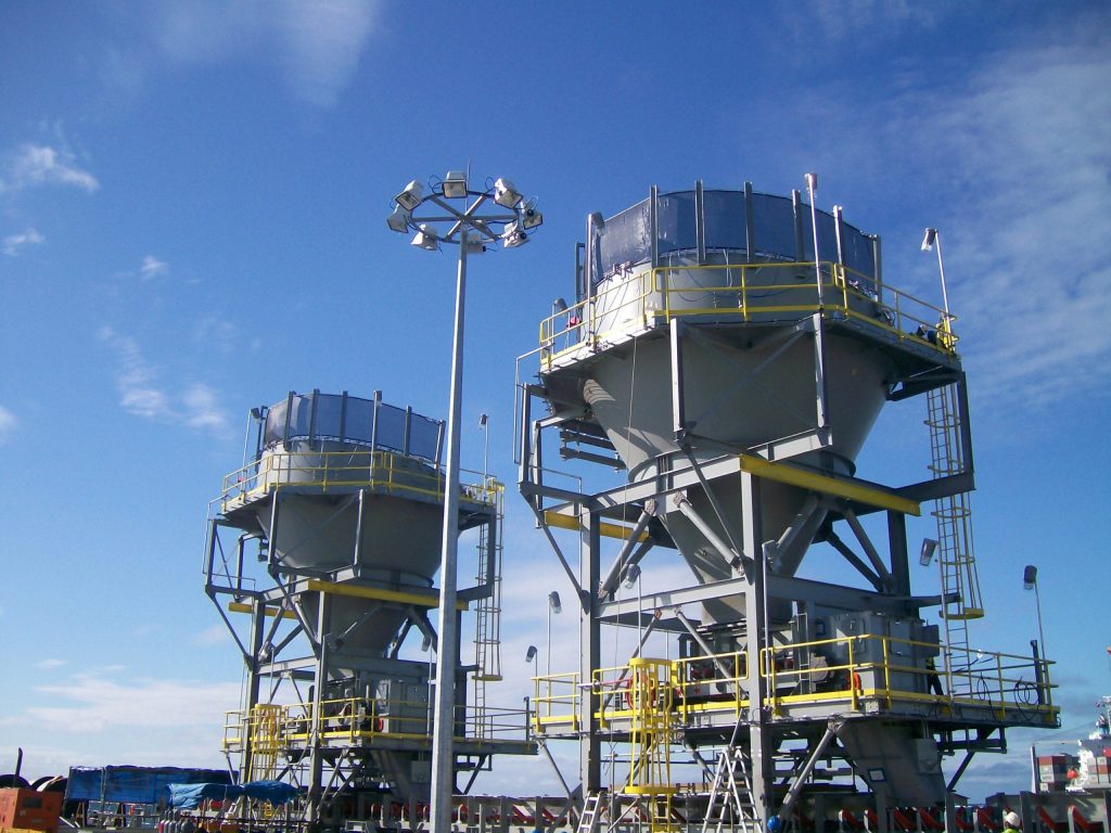 Two large industrial silos with yellow railings and ladders under a clear blue sky