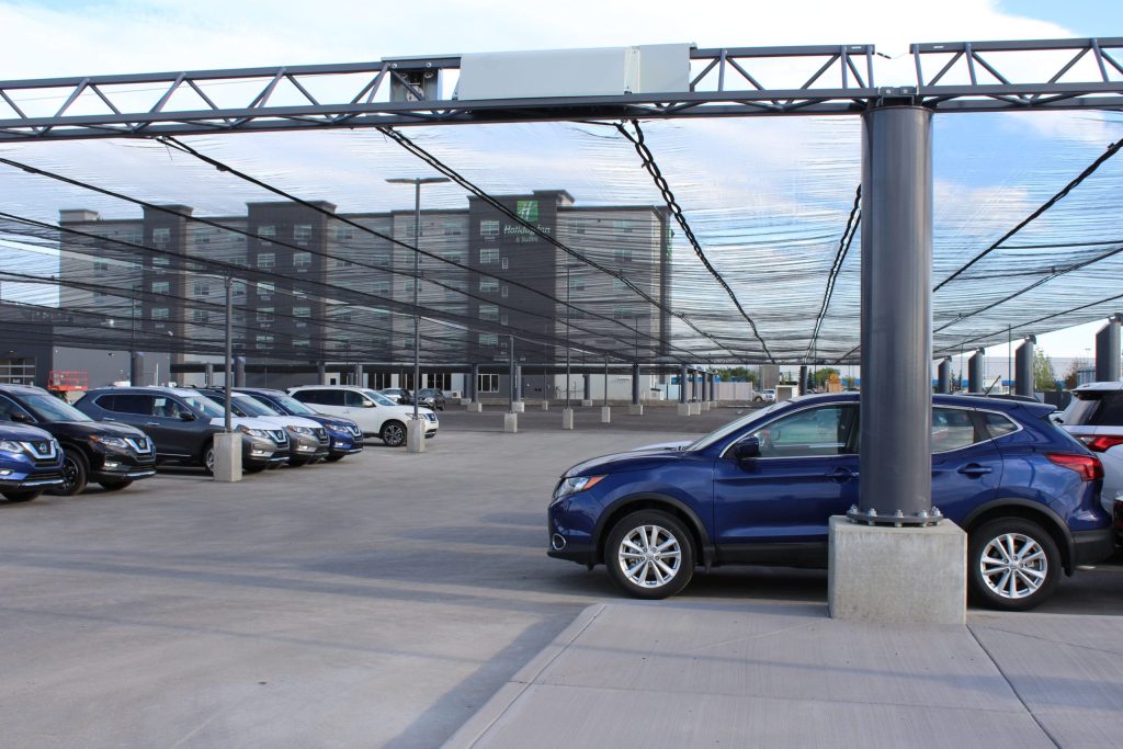 A parking lot with a black mesh canopy covering rows of parked cars