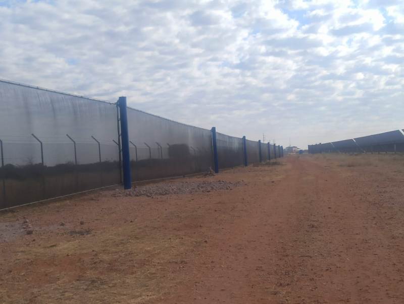 A long, tall wind fence stretches into the distance under a cloudy sky
