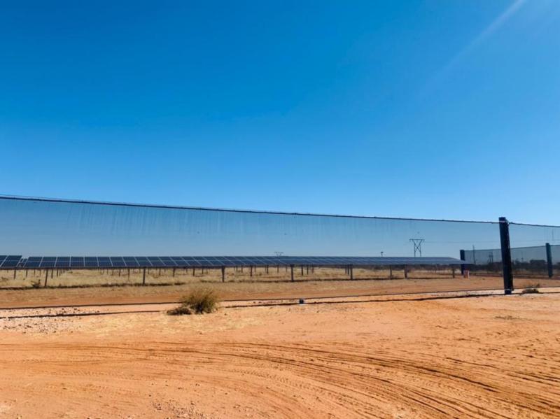 Solar panels behind a chain-link fence in a dry, open landscape