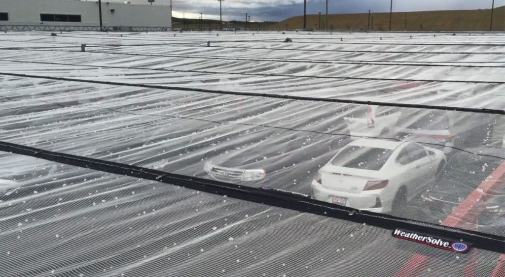 A covered parking lot with a white car and a truck under a hail canopy