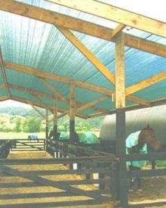A covered horse stable with wooden beams and a translucent blue roof