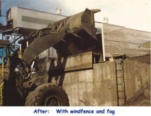 Construction equipment unloading material near a large industrial building, with visible windfence and fog.