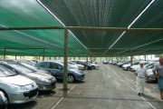 A parking lot with cars shaded by green fabric canopies supported by wooden poles
