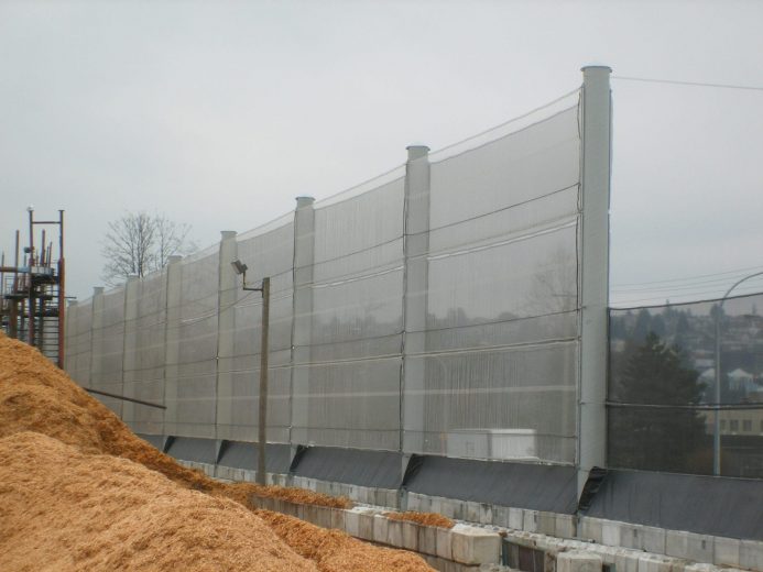 A tall, translucent wind fence stretches along a construction site with piles of dirt