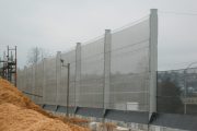 A tall, translucent wind fence stretches along a construction site with piles of dirt