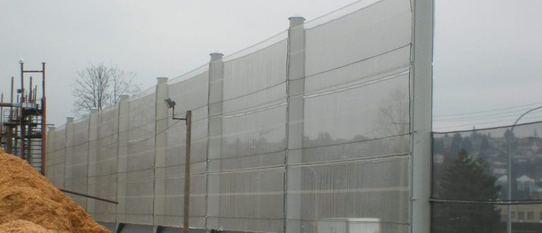 A tall, translucent wind fence stretches along a construction site with piles of dirt