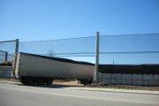A semi-truck trailer is positioned under power lines beside a concrete barrier