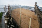 A large pile of grain is covered by a wind fence near a waterfront city