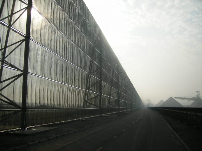 A long industrial fence stretches alongside a road under a hazy sky