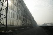 A long industrial fence stretches alongside a road under a hazy sky