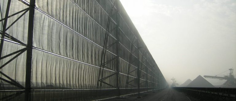 A long industrial fence stretches alongside a road under a hazy sky