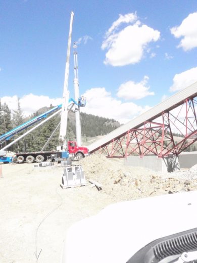 A crane and conveyor belt structure at a construction site with a mountainous backdrop