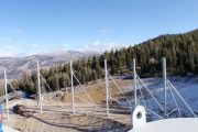 Metal poles and supports installed on a sloped, snowy ground with trees and mountains in the background
