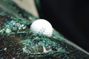 A golf ball rests on shattered glass, likely from a hail impact test