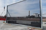 A large industrial wind fence being installed with a crane and worker in safety gear