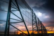 A large industrial fence structure stands against a dramatic sunset sky