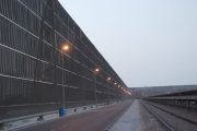 A long industrial wind fence stretches alongside a road and railway tracks