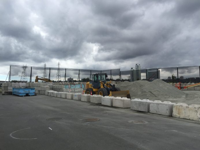 A construction site with heavy machinery and concrete barriers under a cloudy sky