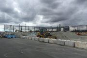 A construction site with heavy machinery and concrete barriers under a cloudy sky