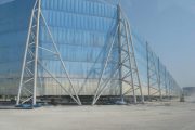 A large, blue, translucent structure supported by a white metal framework stands on a dusty, unpaved surface