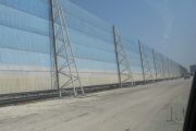 A long, light blue wind fence stretches across a sandy area under a clear sky