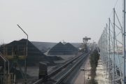 Coal piles and conveyor belts at an industrial site with a large wind fence