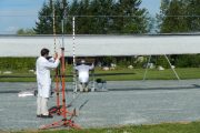 Two scientists in white lab coats work with equipment under a large white canopy outdoors