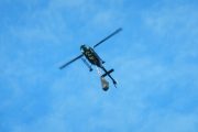 A helicopter flies against a blue sky with a bucket suspended below it
