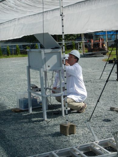A person in a white shirt and hard hat works on equipment under a canopy