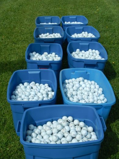 Nine blue bins filled with white golf balls on a grassy field