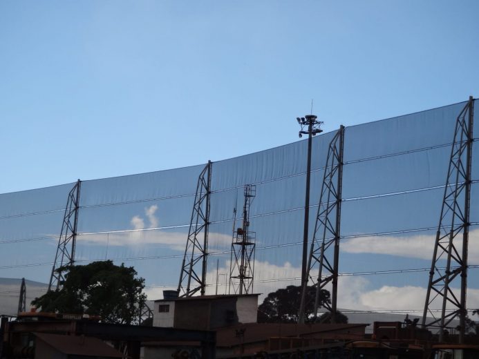 A large industrial wind fence stretches across the image against a clear blue sky
