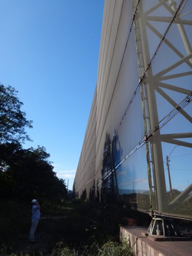 A person in a hard hat stands next to a large industrial wind fence