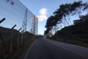 A road curves to the right with a tall fence and trees on either side