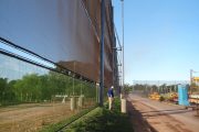 A large wind fence stretches along a dirt road with a person standing nearby