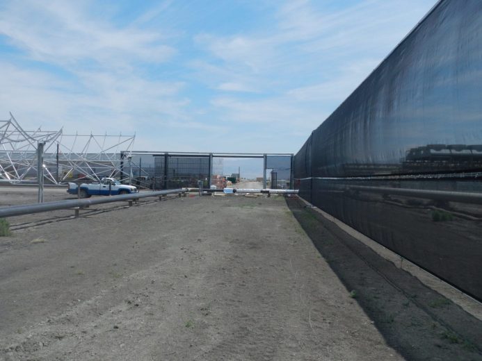 A construction site with a blue truck, metal framework, and a large black fence