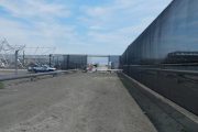 A construction site with a blue truck, metal framework, and a large black fence