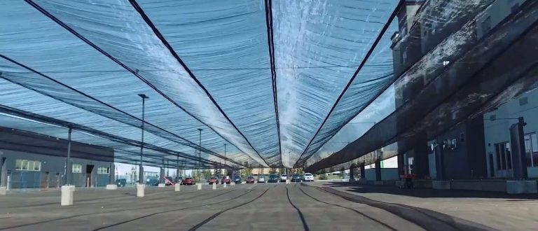 A covered parking area with a translucent blue canopy overhead and cars parked underneath