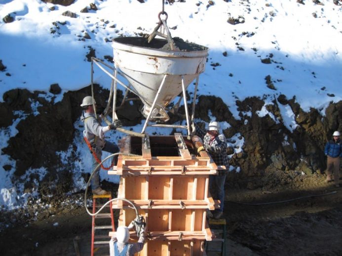 Workers pour concrete into wooden forms at a snowy construction site