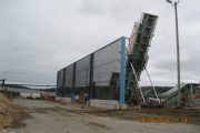A large industrial structure with a conveyor belt leans against a building