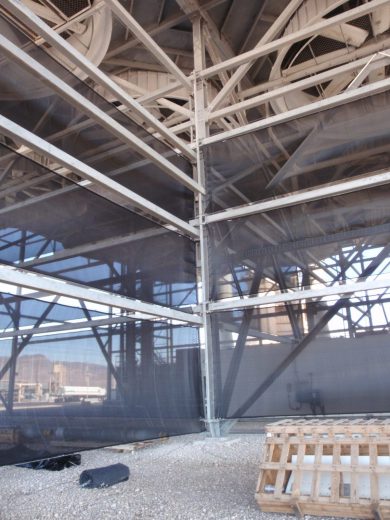 Industrial structure with metal framework and dark mesh panels, gravel ground, and wooden pallet