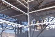Industrial structure with metal framework and dark mesh panels, gravel ground, and wooden pallet