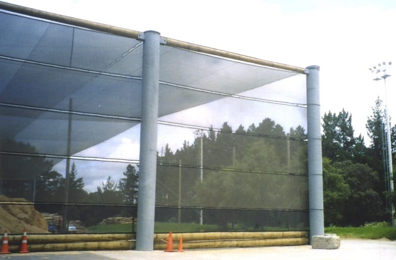 A large, translucent wind fence supported by cylindrical pillars stands outdoors