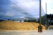 A large pile of wood fiber is covered by a mesh canopy supported by metal poles