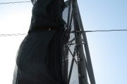 A black mesh wind fence attached to a tall metal frame against a clear sky
