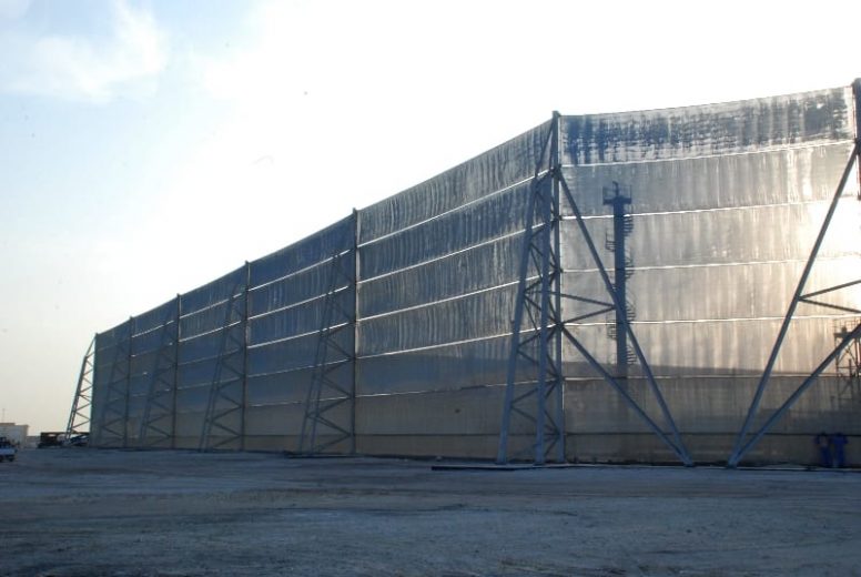 A large industrial wind fence stretches across a flat, dusty area
