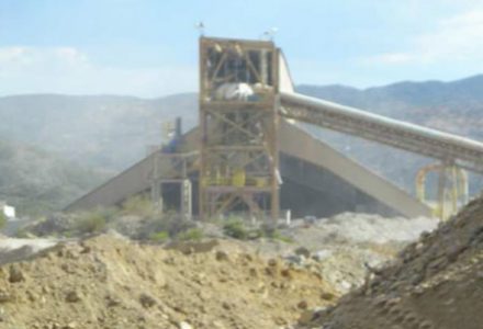 Industrial structure with conveyor belt amidst dirt mounds and mountainous backdrop