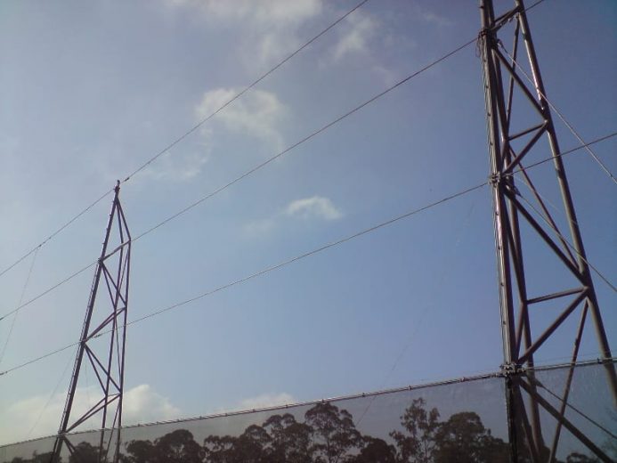 Two tall metal towers with cables against a clear sky and trees in the background